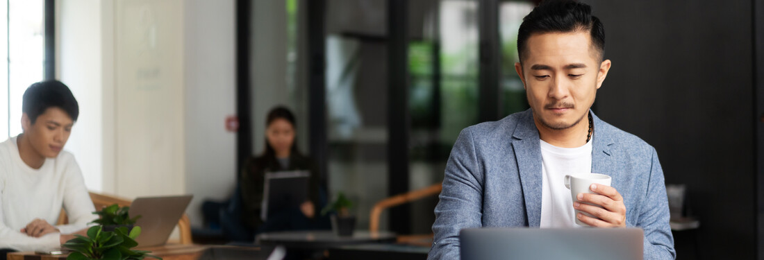 A man seated at a table, focused on his laptop, engaged in work or study in a well-lit environment.