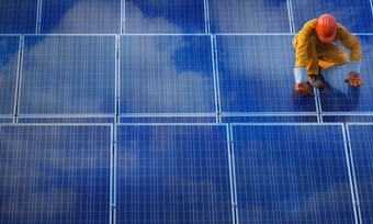 A man in an orange work jumpsuit inspects solar panels