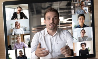 A person using a laptop to video conference with a group of people displayed on the screen.