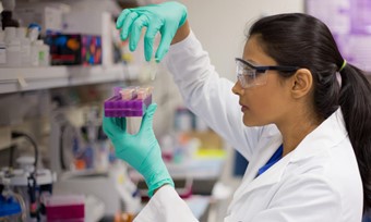 A woman wearing a lab coat inspecting a test tube